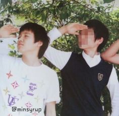 three young men standing next to each other in front of some trees and bushes with their hands on their heads