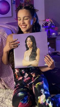 a woman sitting on a bed holding up a photo of herself with her face painted