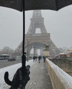 the eiffel tower is covered in snow as people walk under an open umbrella