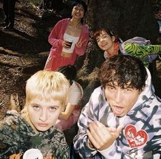 a group of young people standing next to each other in the woods with cups and saucers