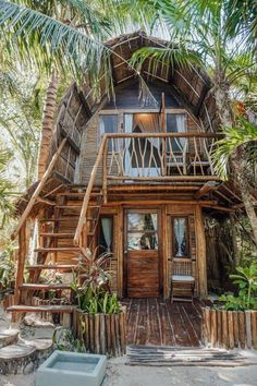 a wooden house with stairs leading up to the front door and second story that is surrounded by palm trees