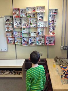 a young boy sitting at a desk in front of a wall with pictures on it