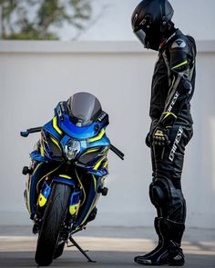 a man standing next to a blue and yellow motorcycle on the street with his helmet on