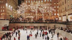 people skating on an ice rink in the city at night with lit up christmas trees