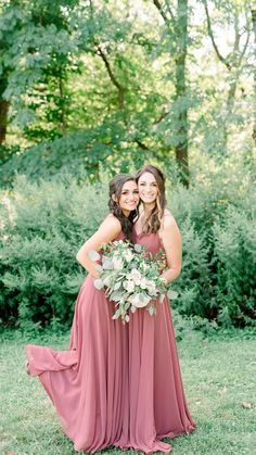 two bridesmaids pose for a photo in front of some trees and greenery