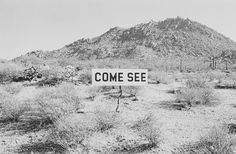 a black and white photo of a sign in the desert with mountains in the background