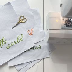 several pieces of white paper with embroidered words on them next to a sewing machine and needle