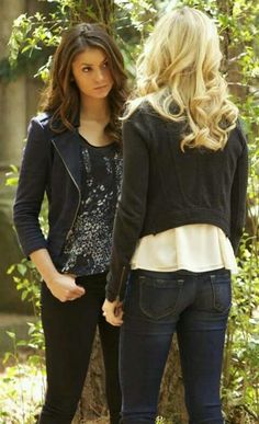 two young women standing next to each other in the woods, one holding her hand