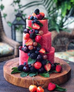 a cake made out of fruit on top of a wooden table next to berries and strawberries