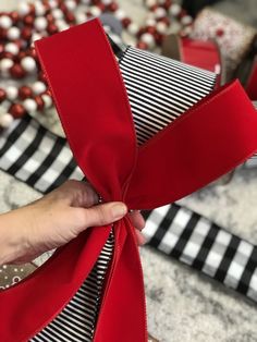 a person is tying a red ribbon on a christmas tree ornament with black and white stripes