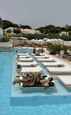 people are lounging on lounge chairs in the pool