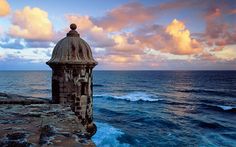 an old tower overlooks the ocean at sunset