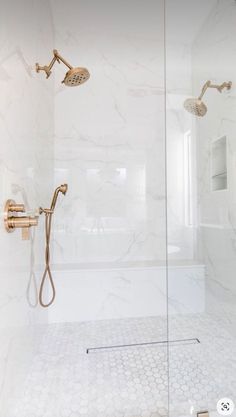 a bathroom with white marble walls and floor, shower head, and hand held shower faucet