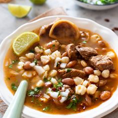 a white bowl filled with meat and bean soup next to a lime slice on the side