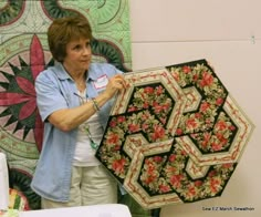 a woman holding up a quilt in front of a wall