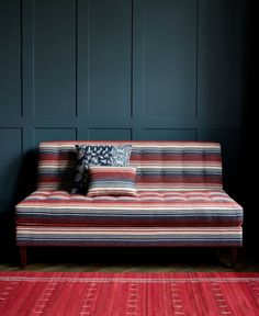 a striped couch sitting on top of a wooden floor next to a red rug and black wall