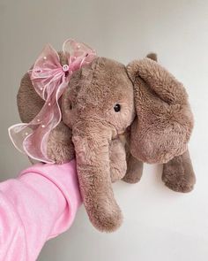 an elephant stuffed animal being held by a person's arm with a pink shirt on