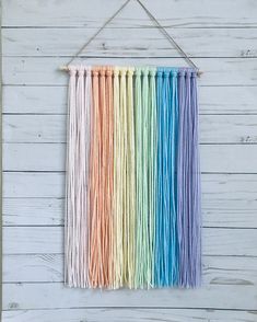 a multicolored wall hanging on a white wooden wall with string attached to it