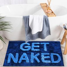 a blue rug that says get naked on it in front of a bathtub with towels