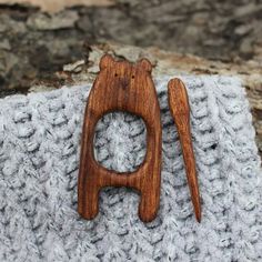 a pair of wooden scissors sitting on top of a gray knitted cloth next to a piece of wood