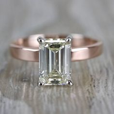 an emerald cut engagement ring on top of a wooden table with a diamond in the center