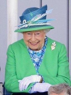 the queen of england smiles as she sits at a table with other people in suits and hats