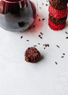 a glass filled with red liquid next to some chocolate pieces and sprinkles