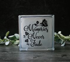 a glass block with the words memories never fade written in black on it next to some leaves