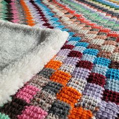 a multicolored knitted blanket laying on top of a bed