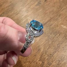 a person holding a ring with a blue topazte surrounded by white and clear diamonds