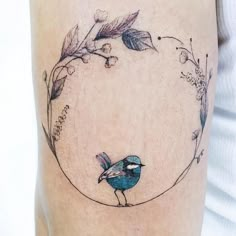 a small blue bird sitting on the side of a woman's leg with flowers and leaves around it