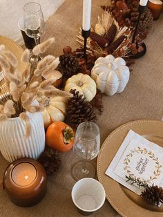 the table is set for thanksgiving dinner with white pumpkins, pine cones and candles