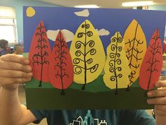 a person holding up a paper cutout with trees on it in front of them