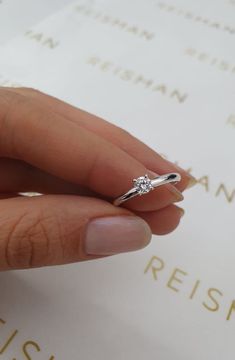 a woman's hand holding a diamond ring on top of a piece of paper