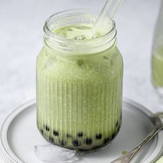 a jar filled with green liquid sitting on top of a plate next to two spoons