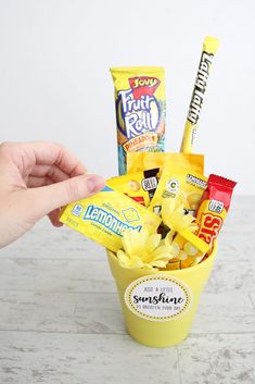 a hand holding a yellow cup filled with candy and candies next to a white wall