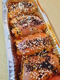 three hot dogs covered in sesame seeds and ketchup on top of tin foil