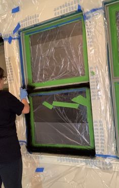 a woman in black shirt and blue gloves painting windows with green paint on the wall