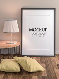 two pillows on the floor next to a framed mockup with your design here sign