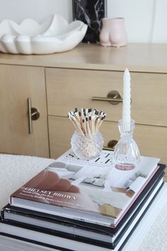 a stack of books sitting on top of a table next to a vase and candle