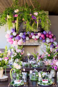 a table topped with lots of flowers and greenery next to a fireplace covered in balloons