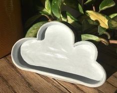 a white heart shaped dish sitting on top of a wooden table next to a potted plant