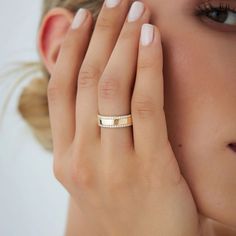 a woman holding her hand up to her face and wearing a gold ring with the word love on it