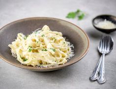 a bowl filled with pasta and parsley on top of a table next to two spoons