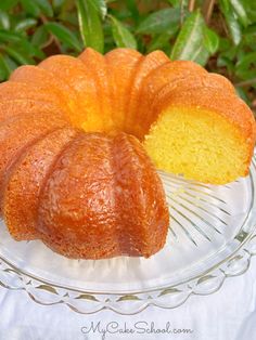 a bundt cake sitting on top of a glass plate next to a green bush