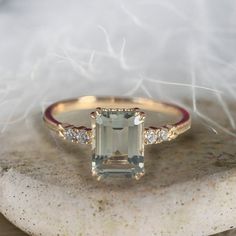 an engagement ring with a large green stone surrounded by small white diamonds on top of a rock