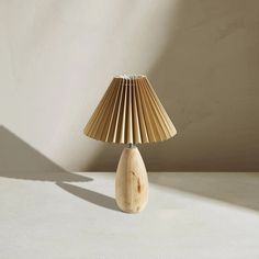 a wooden table lamp with a beige shade on it's base and a white wall in the background