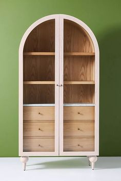 a white bookcase with wooden shelves and drawers in front of a green painted wall