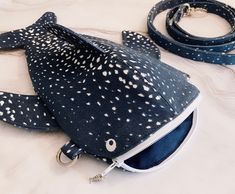 a black and white fish purse on a bed with a leash attached to the bag