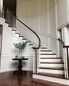 a white staircase with wooden handrails next to a table and potted plant